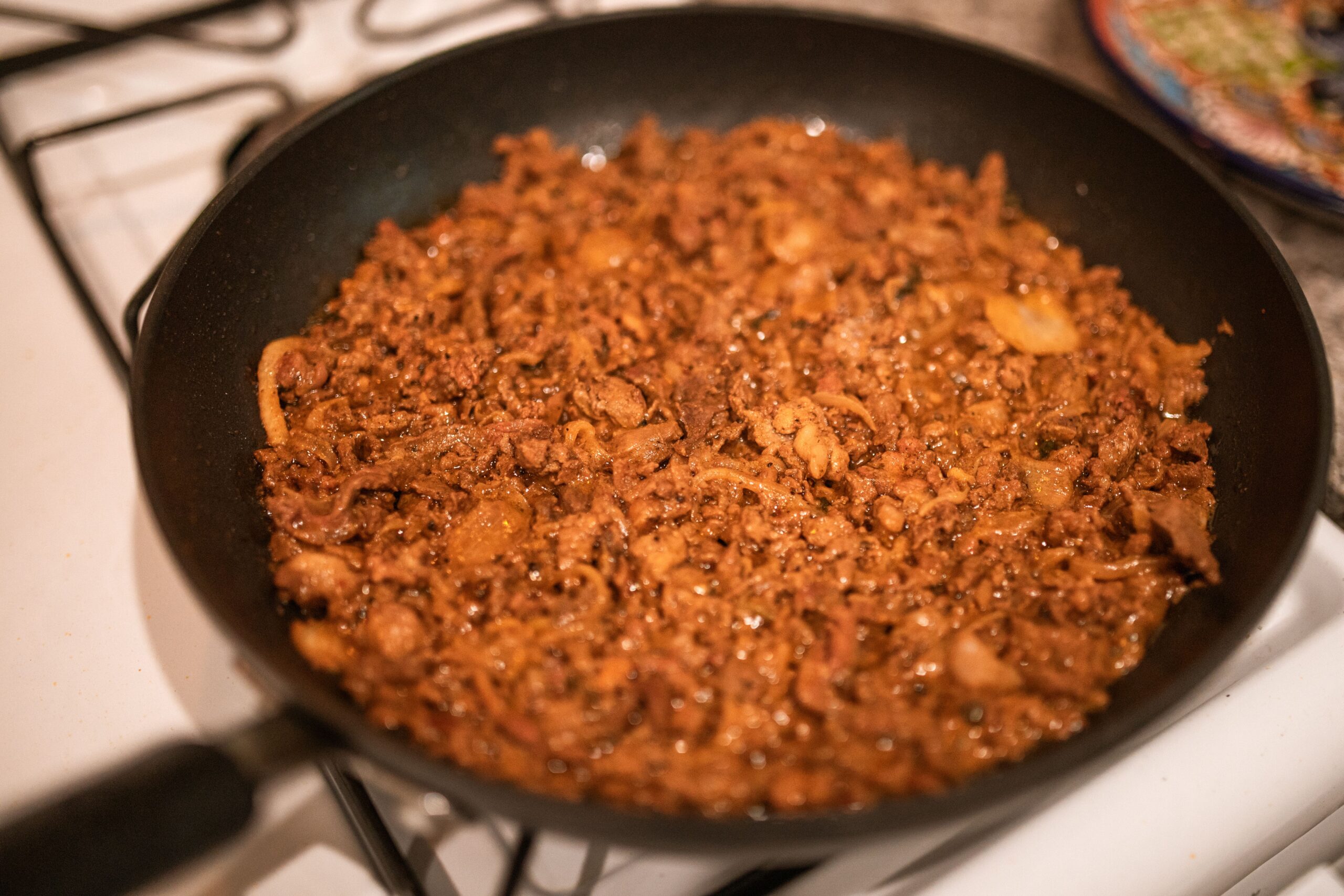Ground beef browning in a skillet, breaking apart while cooking directly from frozen