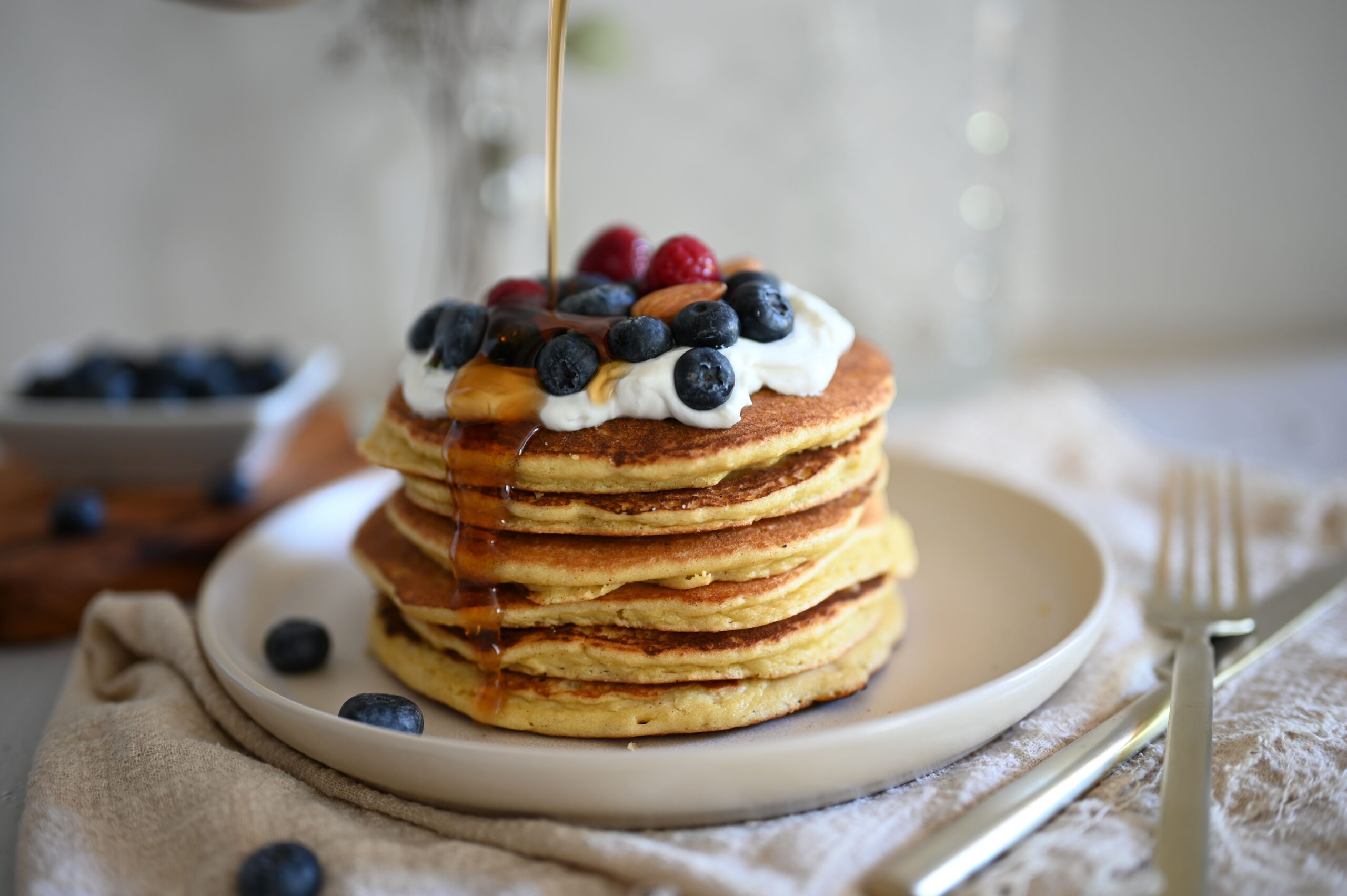 Stack of fluffy golden buttermilk pancakes topped with syrup on a white plate