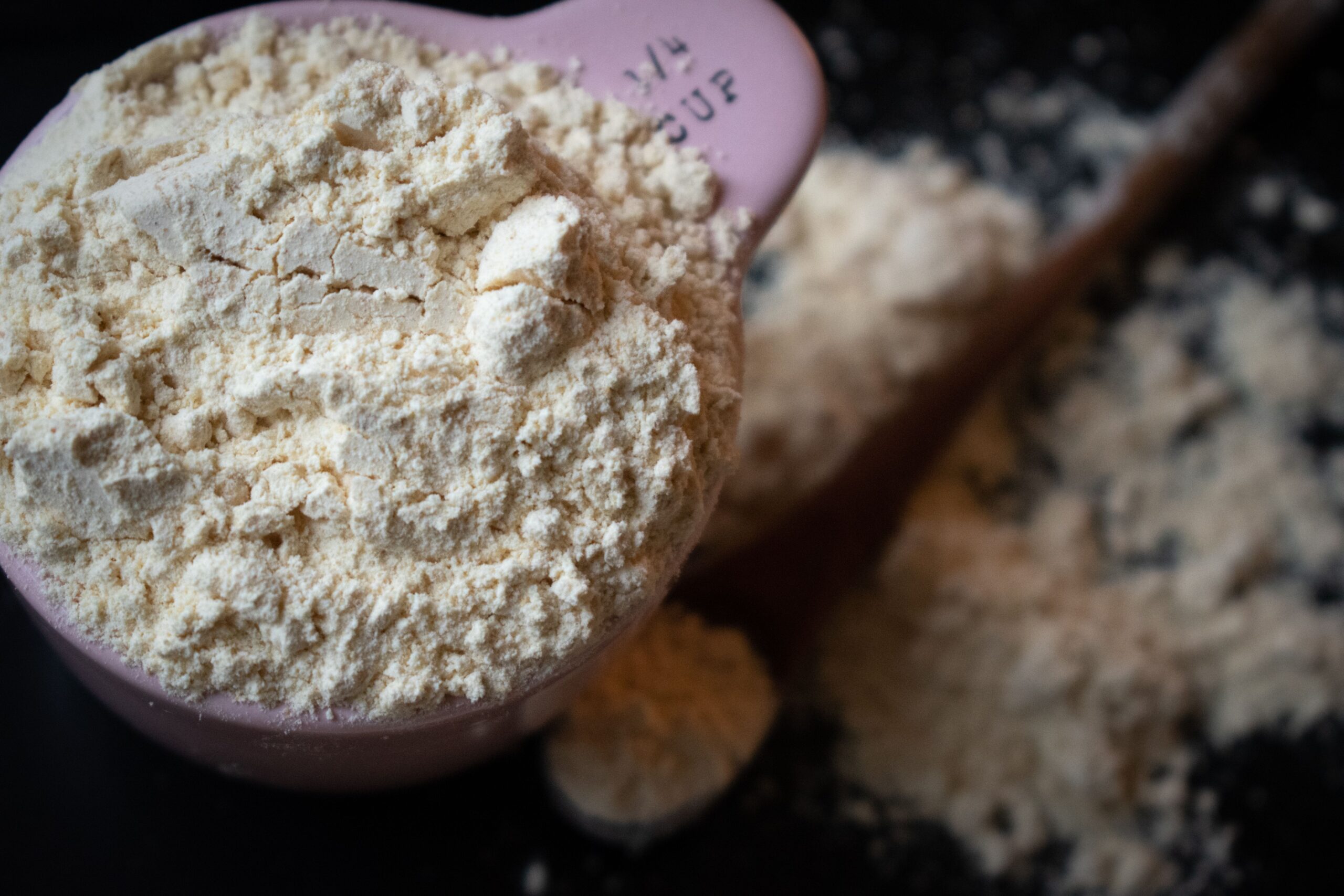 Hand levelling flour in a measuring cup with the flat edge of a knife, demonstrating the correct spoon-and-level technique