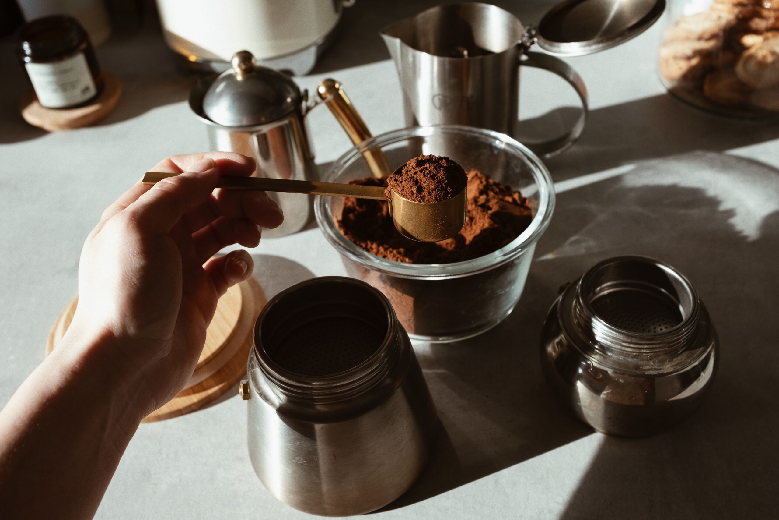 A tablespoon of ground coffee being measured out over a coffee filter basket ready for brewing