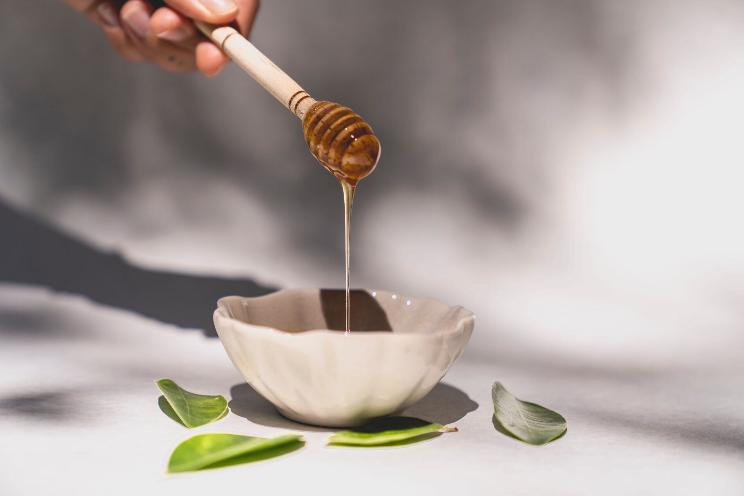 Pouring honey from a jar directly into a mixing bowl on a kitchen scale for precise measurement