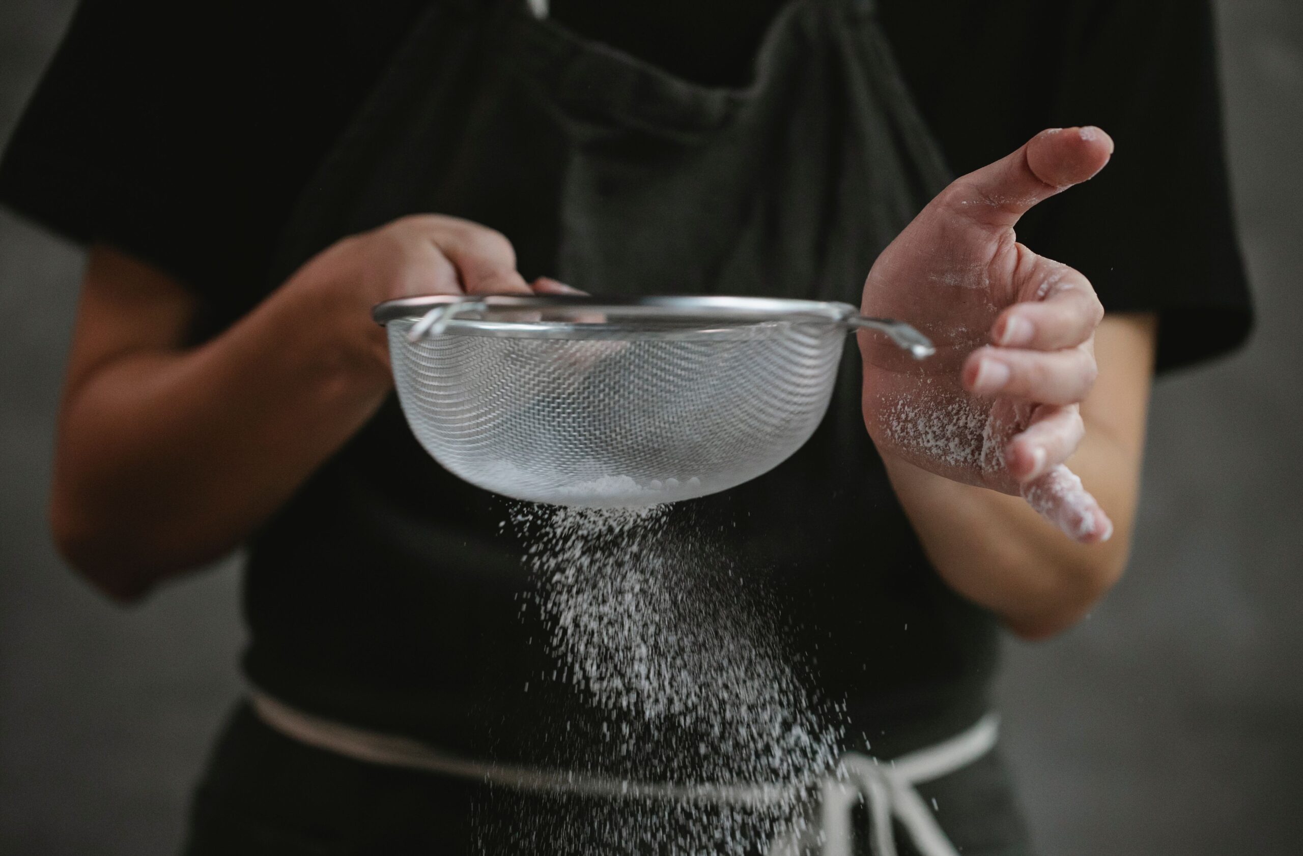 Flour being sifted through a fine mesh sieve into a mixing bowl
