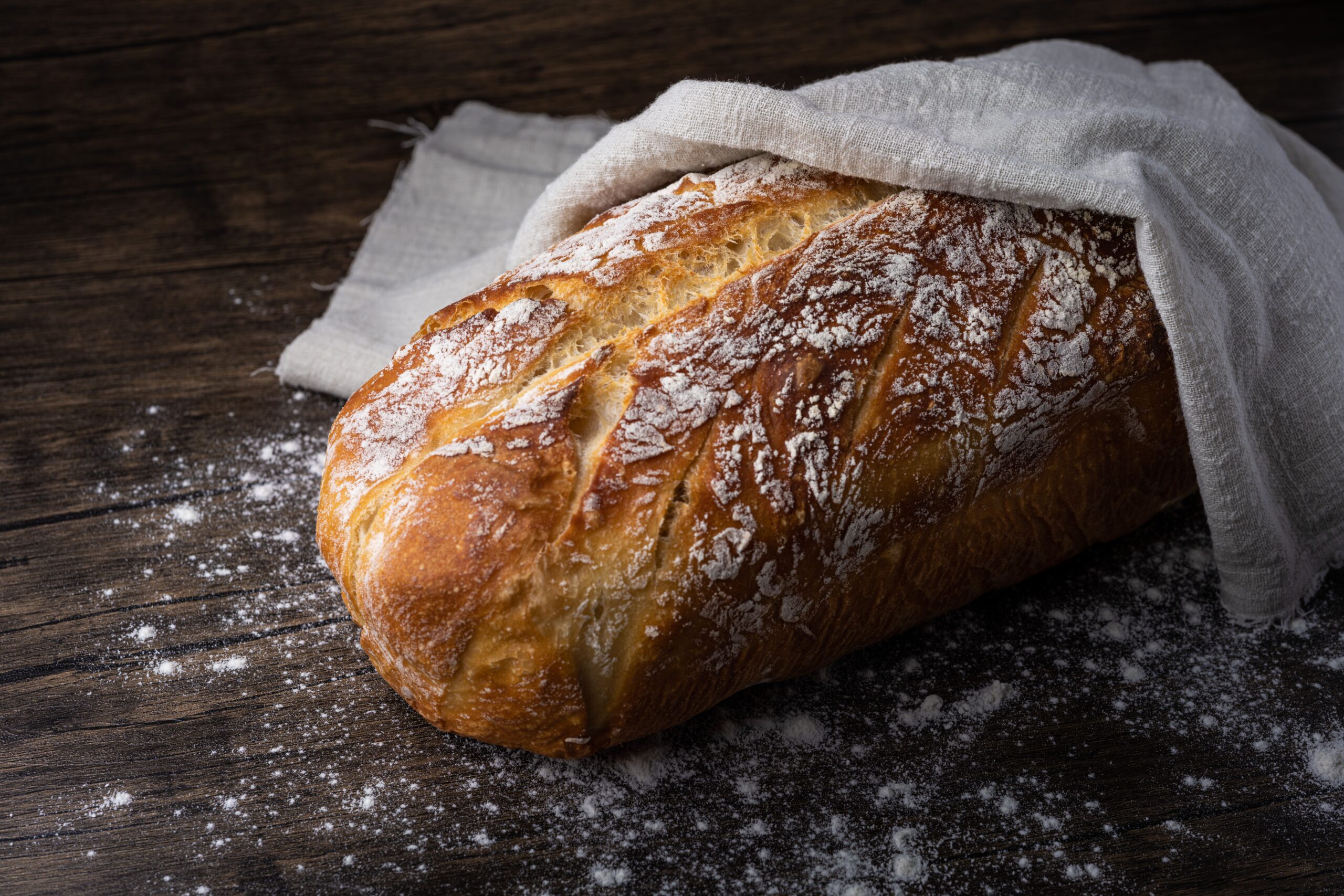 Sourdough loaf dusted with flour on a wooden board, showing rustic crust and open crumb structure