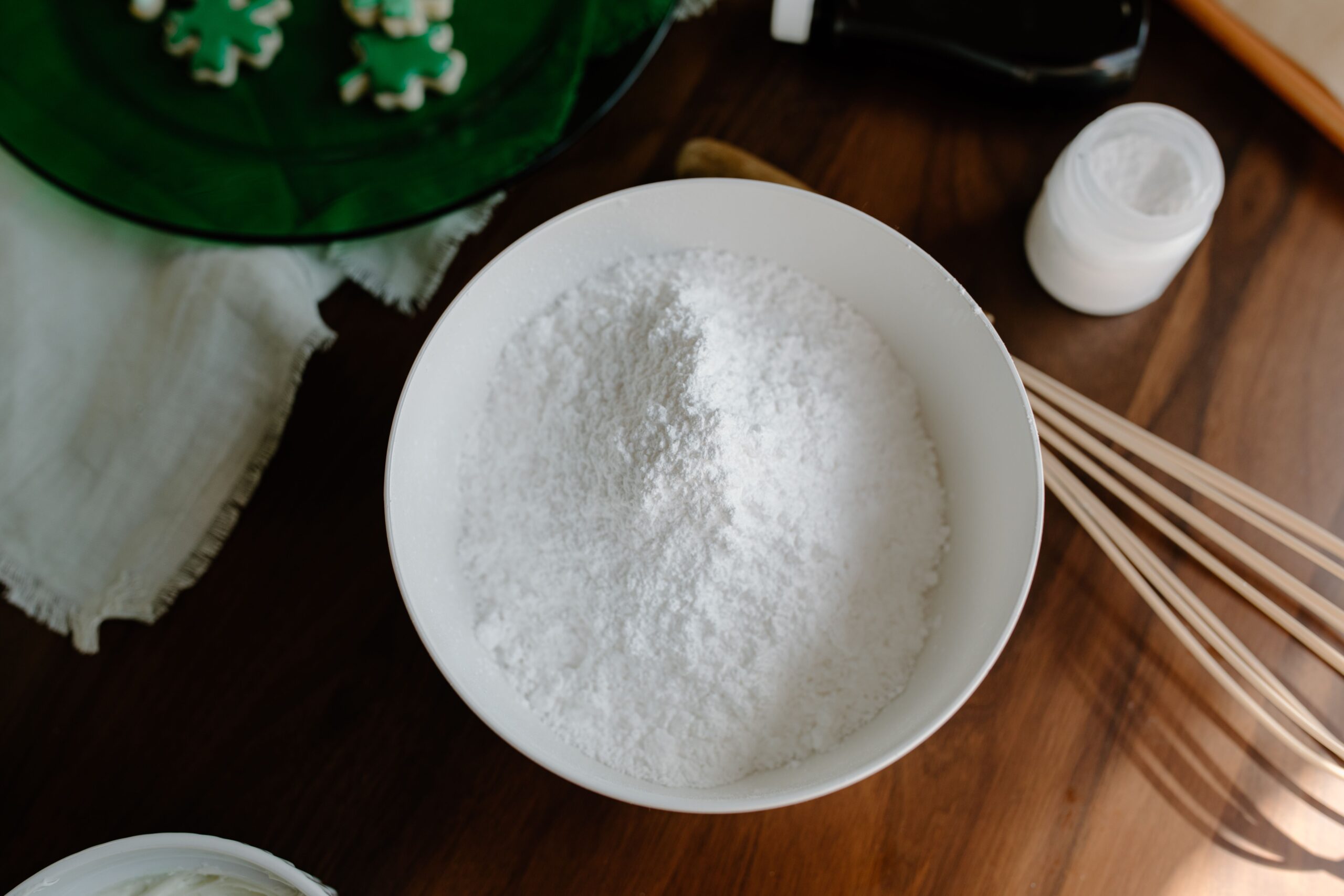 Overhead view of a measuring cup filled with granulated white sugar on a light baking surface